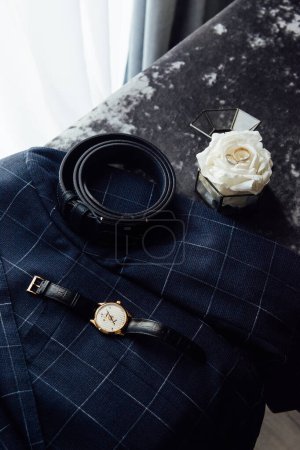 Foto de Aseo detalles de la boda. Reloj, anillos y cinturón colocados en una chaqueta a cuadros. - Imagen libre de derechos
