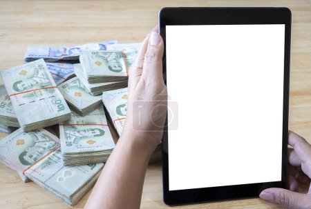 Téléchargez les photos : Gros plan des mains des femmes avec smartphone écran blanc, tablette et pile de billets thaïlandais. concept d'entreprise, de finance, d'épargne, de technologie et de personnes - en image libre de droit