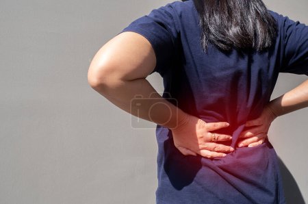 A woman uses her hand to press on the waist due to back pain and waist pain. Pain concept and medical treatment.
