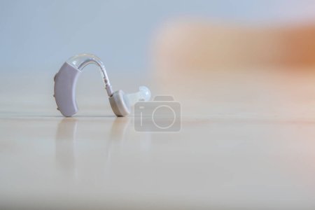 Téléchargez les photos : Gros plan de l'aide auditive pour le traitement de la surdité et de la perte auditive chez l'homme. Aide auditive sur la table en bois légère et mise au point sélective. - en image libre de droit