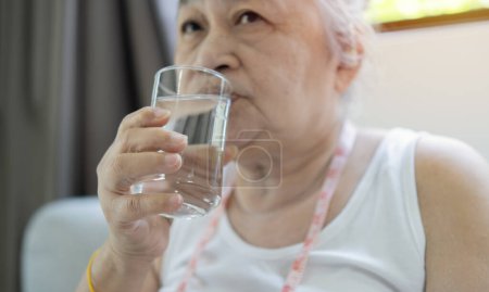 Téléchargez les photos : Concept bien-être. Femme âgée active buvant de l'eau fraîche du verre après l'entraînement sportif domestique, copiez l'espace. Femme sportive rester hydratée pendant la forme physique à la maison - en image libre de droit