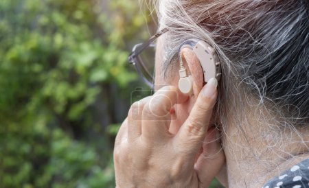 Foto de Primer plano de una mujer mayor insertando y ajustando un audífono en su oído. Enfoque selectivo en el audífono. - Imagen libre de derechos