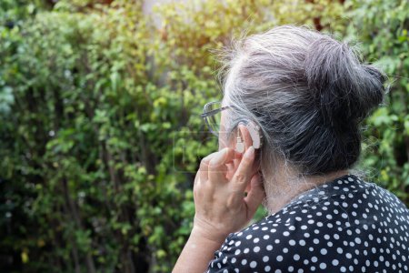 Foto de Audífono. Vista posterior de cerca de una anciana asiática con un audífono en los oídos con fondo natural. Concepto de medicina. - Imagen libre de derechos