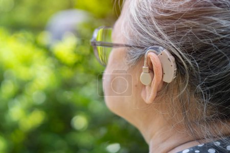 Foto de Mujer de mediana edad con anteojos y el uso de audífonos mientras se sienta en la silla en el jardín en casa. El problema de la audición en la vejez. - Imagen libre de derechos