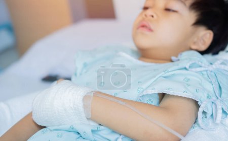 Saline line in the hand of a sick Asian boy lying in a hospital bed. Select focus on saline line. Children's health concept.