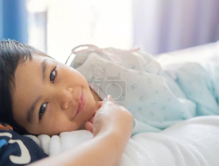 The smile of a sick Asian boy, he looking at the camera while lying down on mother's lap at hospital. Portrait sick boy concept.