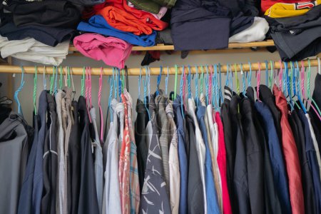 Viele Kleidungsstücke auf Kleiderbügeln. Vielfalt an lässiger Männerkleidung in verschiedenen Farben auf Kleiderbügeln im Männerschlafzimmer.