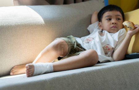 Little Asian boy feet with injured painful left foot with white gauze bandage. Selective focus.