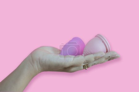Copa menstrual de silicona rosa y púrpura en mano de mujer y aislada sobre fondo rosa. Taza higiénica, espacio para copiar.