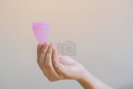 Enfoque selectivo de la mano de la mujer sosteniendo la copa menstrual sobre fondo beige claro. Concepto de salud de las mujeres, cero residuos alternativos