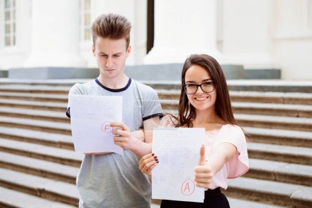 Photo for Two students with test results. Happy female student have received excellent A grade, but her male friend have failed test and have received low mark for his work - Royalty Free Image