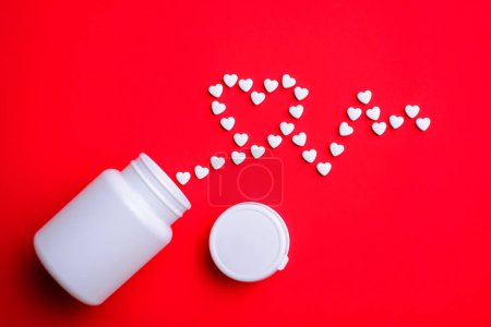 Foto de Concepto de pastillas para el corazón. Pequeñas píldoras blancas en forma de corazón símbolo de forma cardiograma sobre fondo rojo - Imagen libre de derechos