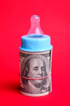 Photo for Nipple of baby milk bottle on a roll of dollar cash against red background. Concept of high price of bringing up - Royalty Free Image