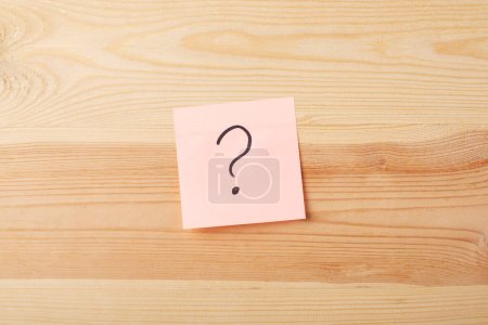 Question mark on a sticky note against wooden background