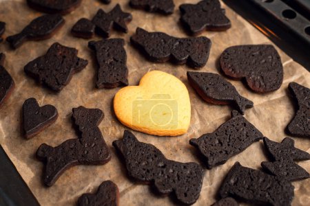 Galleta sabrosa en forma de corazón en medio de otros panes cortos negros quemados de diferentes formas en la bandeja para hornear. Navidad hornear, amor símbolo de supervivencia.
