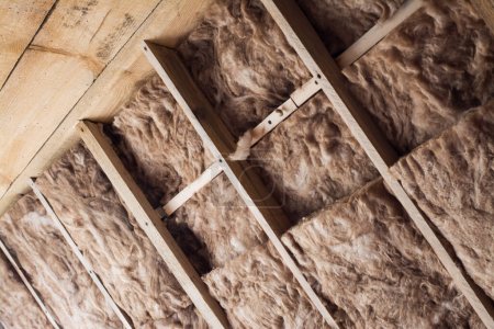 Photo for Glass wool in a wooden frame on a inclined wall near the wooden ceiling at attic. Warming the house with fiberglass. - Royalty Free Image