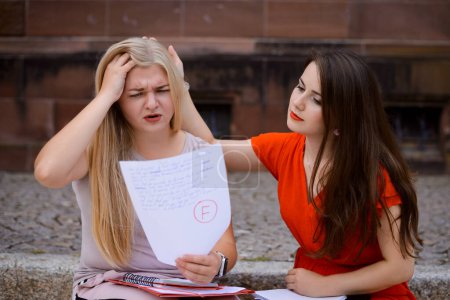 Photo for Student girl with low academic performance has received bad mark for examination, got F grade, failed test. Her friend tries to console and comfort friend in difficulties - Royalty Free Image