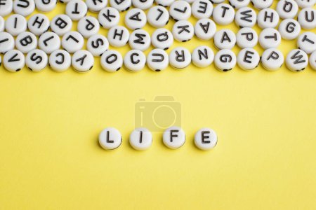 Téléchargez les photos : The word LIFE made of white plastic blocks on yellow background with many letters on the top - en image libre de droit