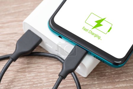 Téléchargez les photos : Powerbank charging smartphone battery on the table, close up picture. Fast charge, modern technologies, hi-tech devices - en image libre de droit