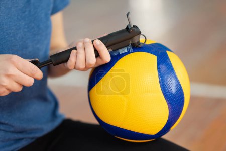 Close up of girl inflating new volleyball ball with hand pump on court before training. Just bought professional ball for training and volleyball competition