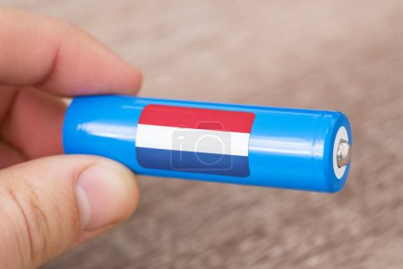 Foto de Batería recargable de iones de litio en la mano de un hombre con pegatina de bandera holandesa. Produce baterías de litio en Holanda - Imagen libre de derechos
