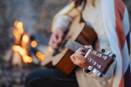 Photo for Close up of a girl playing the guitar near bonfire. Playing the guitar outdoors on nature, having good time with friends near the fire - Royalty Free Image