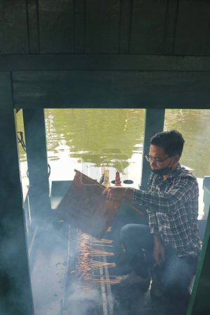 Photo for West Java - Indonesia, October 16th, 2022. Satay Maranggi in grilling place with smoke by people at Floating Market. Traditional satay made from beef skewers with soy sauce, - Royalty Free Image