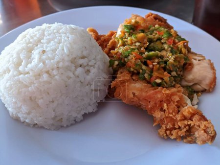 Photo for Nasi ayam geprek or Spicy Geprek chicken rice culinary served on a round white plate. Most favourite dish in Indonesia. - Royalty Free Image