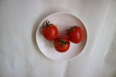 Photo for Three red ripe tomatoes on a white plate and a white background. - Royalty Free Image