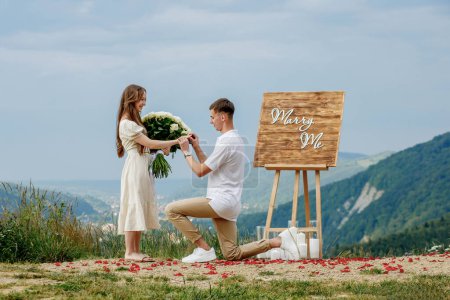 Offer in the mountains. A guy puts a ring on his bride while standing on his knee. Happy couple. Marry me. Good luck with the proposal.