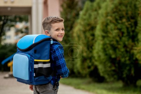 Téléchargez les photos : Portrait d'écolier en chemise bleue avec un sac à dos et des manuels scolaires. Petit écolier. Première année. - en image libre de droit