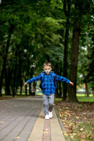 Photo for Boy of school age with a blue backpack goes to school in the park. - Royalty Free Image