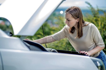 Photo for Confused female driver standing outside her car with the hood up looking at the broken engine - Royalty Free Image