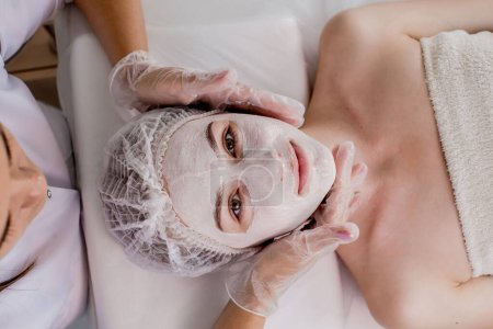 Téléchargez les photos : Woman in moisturizing anti-wrinkle mask. A woman is lying down, resting in a beauty salon. SPA procedures at home or in a cosmetology center. - en image libre de droit