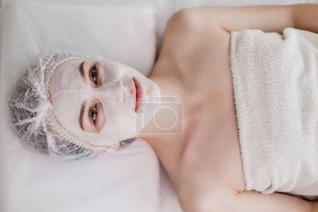 Téléchargez les photos : Woman in moisturizing anti-wrinkle mask. A woman is lying down, resting in a beauty salon. SPA procedures at home or in a cosmetology center. - en image libre de droit