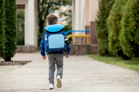 Une petite élève avec un sac à dos bleu va à l'école.