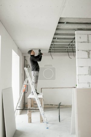 The worker attaches plasterboard on metal frame. Installation of ceiling.