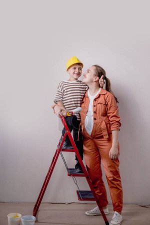 Photo for Home repairs. Mom helping her son paint the wall with a roller. The boy paints the wall of the apartment. New house renovation concept - Royalty Free Image
