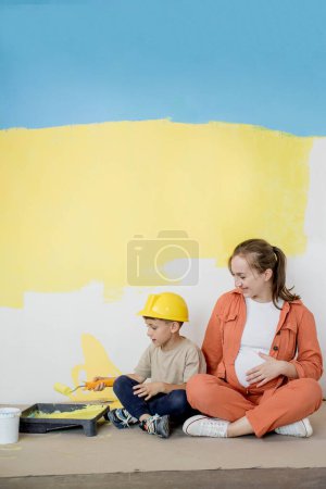 Photo for Home repairs. Mom helping her son paint the wall with a roller. The boy paints the wall of the apartment. New house renovation concept - Royalty Free Image