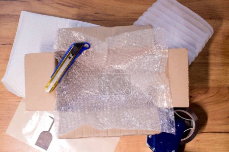 Téléchargez les photos : Open box with wrapped items, adhesive tape, scissors, paper and bubble wrap on wooden table, flat lay. - en image libre de droit