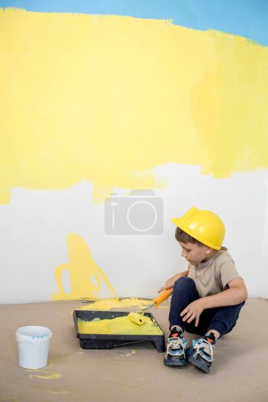 Photo for Cute boy with a paint roller. Happy kid helps parents to paint wall. New house for family - Royalty Free Image