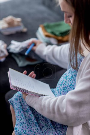 Embarazada mujer escribiendo lista de embalaje para el hospital de maternidad en casa, primer plano