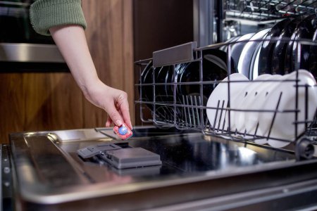 Dishwasher tablet in a woman's hands against the background of an open dishwasher.