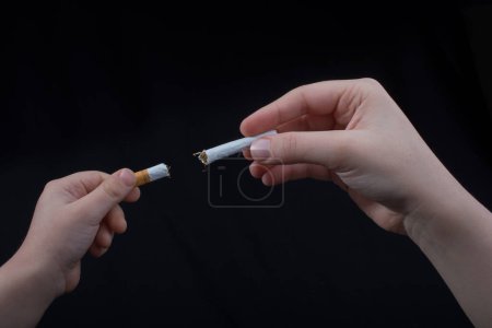 Téléchargez les photos : La main casse une cigarette sur un fond noir - en image libre de droit