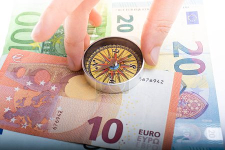Foto de Brújula en mano sobre billetes en euros con dirección a la financiación de la moneda europea - Imagen libre de derechos