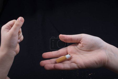 Téléchargez les photos : La main casse une cigarette sur un fond noir - en image libre de droit
