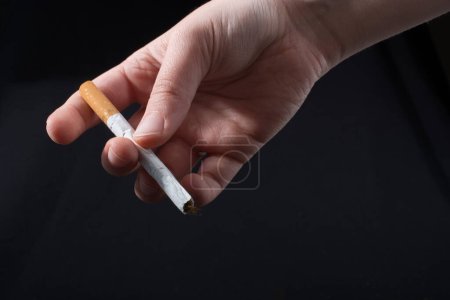 Téléchargez les photos : La main donne la cigarette sur un fond noir - en image libre de droit