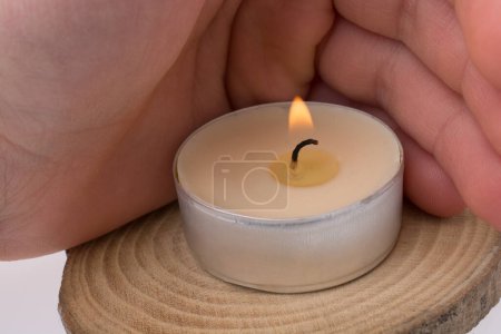 Photo for Hand protecting the burning candle placed  on piece of wood - Royalty Free Image