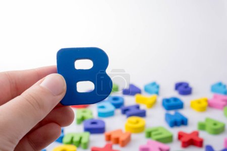 Foto de Letra B en la mano junto a bloques de letras de alfabeto de colores dispersos al azar - Imagen libre de derechos