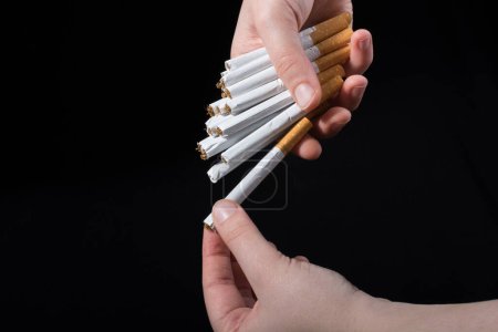 Téléchargez les photos : La main distribue des paquets de cigarettes sur fond noir - en image libre de droit